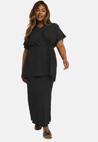 Ensemble en deux pièces texturé noir, comprenant un haut ample à manches courtes avec une taille à nouer et une jupe longue assortie avec des fentes sur les côtés.
