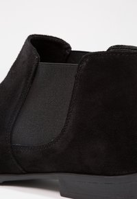 Stivale alla caviglia in suede nero con pannelli elastici laterali e suola nera piatta. Texture liscia e linee pulite, progettato per un'agevole indossabilità.