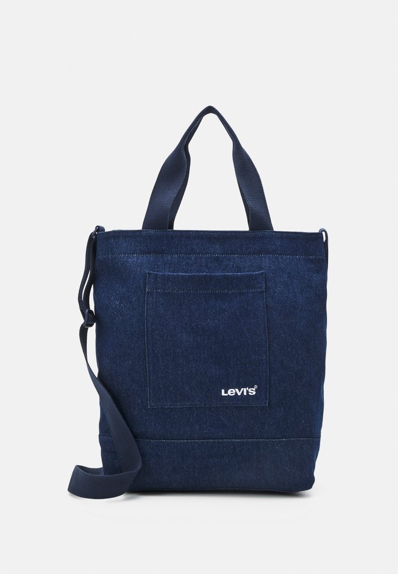 Denim tote bag in dark blue, featuring dual shoulder straps, a front pocket, and a white logo on the lower right corner. Versatile design.