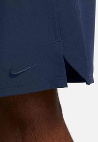 Navy blue sports shorts made of lightweight fabric, featuring a side vent, stitched hem, and a small embroidered Nike logo.