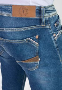 Jeans de mezclilla en azul medio con un parche de cuero en la cinturilla. Presentan cinco bolsillos, costuras a tono y un corte moderno.