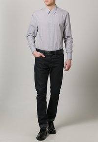 Lys grå langærmet skjorte med knaplukning, parret med mørk denim jeans. Sort bælte og polerede sorte sko. Minimalistisk design.