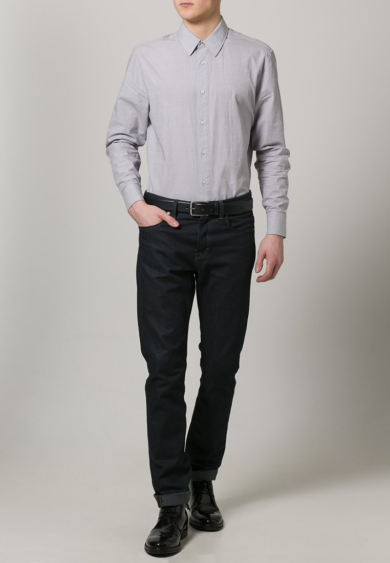 Lys grå langærmet skjorte med knaplukning, parret med mørk denim jeans. Sort bælte og polerede sorte sko. Minimalistisk design.