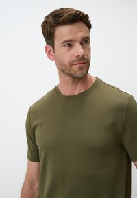 T-shirt verde oliva in un tessuto morbido, con maniche corte, scollo rotondo e una texture liscia senza motivi o dettagli visibili.