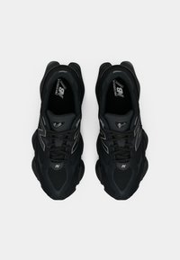 Baskets de sport noires en matériau mesh et synthétique, avec un bout arrondi, des accents de logo contrastants et une semelle rembourrée.