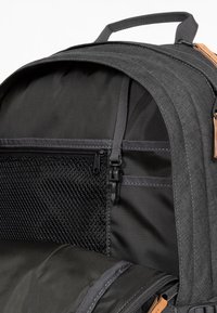 Šedý batoh s vnitřkem se síťovou zipovou kapsou, nastavitelnými popruhy a hladkým, texturovaným materiálem. Obsahuje kožené detaily a odolný design.