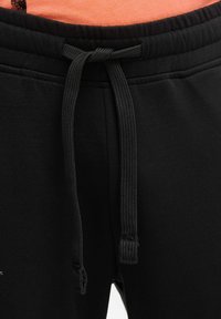 Schwarze Jogginghosen mit elastischem Bund und schwarzem Tunnelzug, mit glatter Textur und einem kleinen Logodetail in der Nähe der Tasche.