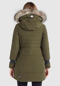 Olivgrön parka med huva i päls, quiltat mönster, ribbade mudd, och en sidetikett med logodetalj.