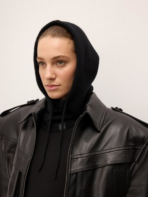 Chaqueta de cuero negro con un diseño estructurado, llevada sobre un suéter negro con capucha de punto negro. Textura suave y detalles de costura sutiles.
