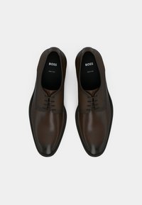 Braune Leder-Herrenschuhe mit glatter Oberfläche, Schnürdesign, dezenten Prägungen am Obermaterial und schwarzer Gummisohle.