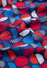 Tissu bleu avec un motif de demi-cercles rouges, bleus et blancs, de cercles et de triangles rayés, présenté avec des plis délicats.