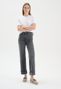 Jeans grigi alti in vita con fit dritto, risvolti, abbinati a una t-shirt bianca a maniche corte e scarpe beige. Design semplice, look casual.
