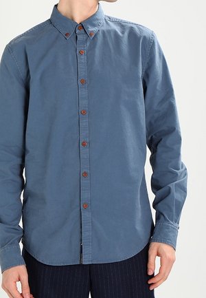 Skjorte med knapper i bomuld i marineblå med en blød tekstur. Har en rundet krave og brune knapper ned foran.