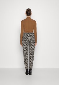 Bruine geribde lange mouw top gecombineerd met zwart-witte geprinte broek. De outfit heeft een aansluitend ontwerp en hoge zwarte laarzen.