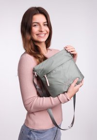 Hellgrünes, strukturiertes Umhängetasche mit pinkem Reißverschlussdetail. Verfügt über einen verstellbaren Riemen und hat eine rechteckige Form.