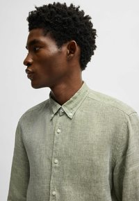 Camicia in lino verde chiaro con colletto button-down e patta abbottonata. Presenta un tessuto testurizzato e una vestibilità standard con maniche lunghe.