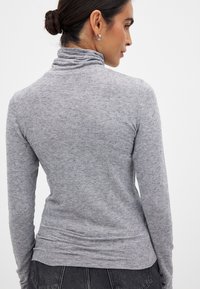 Grå, långärmad polotröja i mjukt, strukturerat tyg. Har en figurnära silhuett med subtila rynkor vid nedre ryggen.