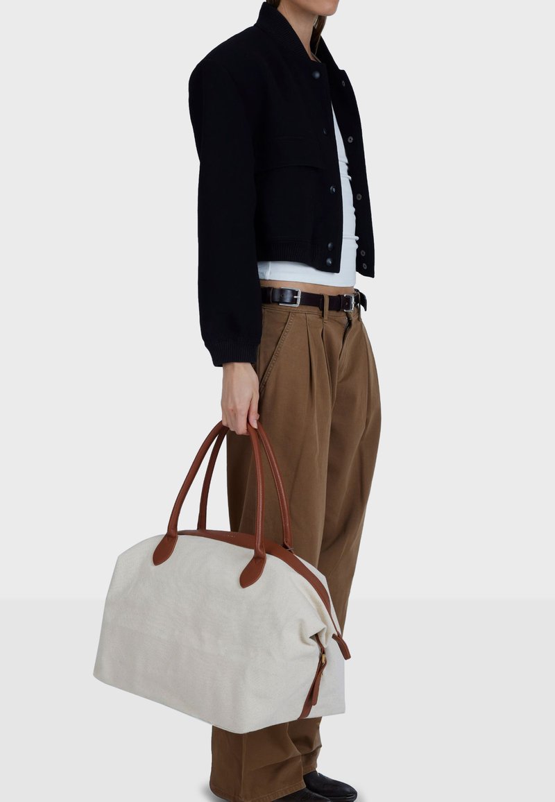 Sac de voyage en toile écrue avec accents et poignées en cuir marron, doté d'une fermeture éclair et d'une forme douce et structurée.