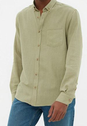 Chemise verte claire à manches longues avec un devant à boutons, comportant une poche poitrine unique et des boutons en bois. Coupe décontractée avec un tissu texturé.