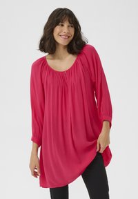 Blouse rose vif avec un décolleté arrondi, un détail froncé, des manches trois-quarts et une coupe ample, fabriquée en tissu texturé léger.