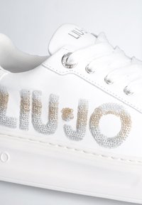 Sneaker bianco con tessuto testurizzato, caratterizzato da "LIU•JO" in glitter argento e oro. Punta rotonda, suola piatta e occhielli in metallo per i lacci.