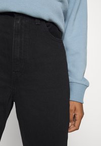 Jeans in denim nero con texture liscia, vita alta e tasche laterali, abbinati a una felpa azzurro chiaro con polsini a coste.