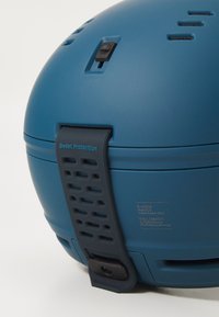 Modrá prilba s ventilačnými otvormi, nastaviteľný popruh označený "Sweet Protection" a embosovaný text, ktorý označuje technológiu dvojitej hustoty.