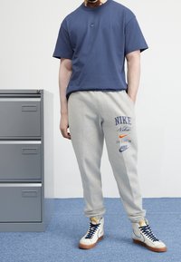 Tmavě modré bavlněné tričko s malým logem Nike, světle šedé tepláky se barevným brandingem Nike a bílé vysoké tenisky s námořnickými akcenty.