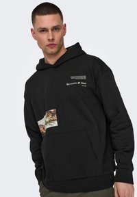 Sudadera negra con un bolsillo frontal, que presenta una sección impresa que representa la obra "La Creación de Adán" y texto en blanco. Material de mezcla de algodón.