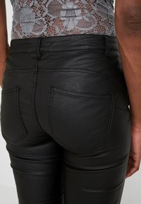 Svarta leggings i konstläder med en slät yta, utrustade med två bakfickor och synlig sömdetalj längs sömmarna.