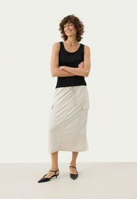 Sort tanktop med rund halsudskæring, parret med en beige mid-længde nederdel med snoreliv og sidelommer; båret med sorte hæle.