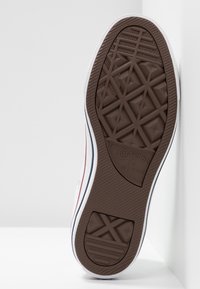 Brązowa gumowa podeszwa sportowa z wzorem diamentowym, białe boki z czerwonymi i niebieskimi paskami oraz teksturowany design na pięcie.