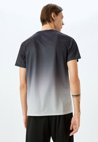 Camiseta atlética de manga corta con un degradado de negro a gris, tejido texturizado y cuello redondo. Sin logotipos ni patrones visibles.