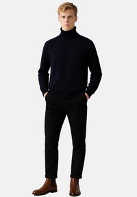 Námořnický rolák vyrobený z žebrované tkaniny, kombinovaný s černými kalhotami a hnědými koženými chelsea botami, vystavený na neutrálním pozadí.