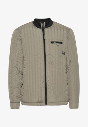 Chaqueta ligera acolchada en beige, con cierre frontal, cuello de canalé y bolsillo en el pecho con cremallera, hecha de un tejido sintético suave.