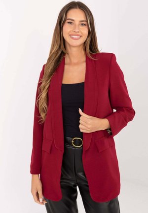 Roter maßgeschneiderter Blazer mit Schalkragen, zwei Fronttaschen und langen Ärmeln, kombiniert mit einem schwarzen Top und hochtaillierter schwarzer Hose.