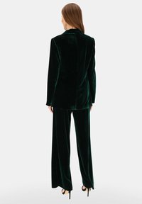 Zielony aksamitny garnitur z długim żakietem i spodniami o szerokich nogawkach. Tkanina ma miękką fakturę, gładkie wykończenie oraz eleganckie detale w projekcie.