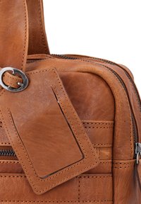 Pruun nahast kott, millel on tekstureeritud viimistlus, sisaldab hõbedast riiviga pandlat ja kudumisega ääristatud pagasitemplit. Nähtav tõmblukuga kott.