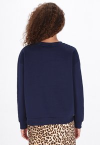 Donkerblauw sweatshirt met ronde hals en lange mouwen, met een comfortabele pasvorm. Het kledingstuk wordt gecombineerd met een rok met luipaardprint.