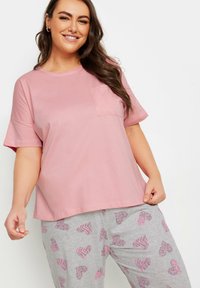 Rosa t-shirt med kort ärm och bröstficka, matchad med grå pyjamasbyxor med ett mönster av hjärtan i rosa och svarta färger.