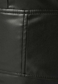 Närbild av svart lädermaterial med detaljerad sömnad längs vertikala och horisontella sömmar.