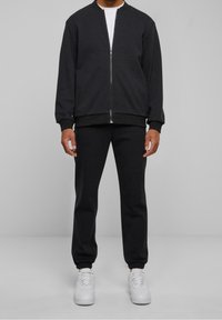 Zwarte bomberjack met ritssluiting en geribbelde manchetten, gecombineerd met bijpassende taps toelopende joggers en witte sneakers. Soepele stof, casual pasvorm, minimalistisch ontwerp.