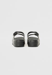 Black platform sandals with two adjustable straps featuring a textured surface and a thick rubber sole. Rear view shows arch support.