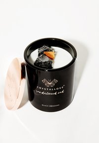Bougie noire avec une finition brillante et un couvercle en or rose, contenant de la cire blanche, de l'obsidienne noire et un accent en bois de santal à l'intérieur.