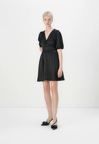 Svart kort kjole med V-hals, puffete ermer og innsvingt midje. Glatt stoff med myk glans og knyttedetalj foran.