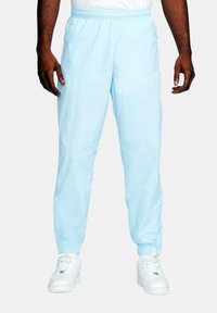 Ljusblå joggers med elastisk midja och mudd, med en liten logotyp på sidan, i kombination med vita sneakers.