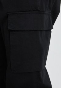 Schwarze Cargo-Hosen mit einer aufgesetzten Tasche an der Seite, aus strapazierfähigem Baumwollmaterial mit glatter Textur und verstärkten Nähten.