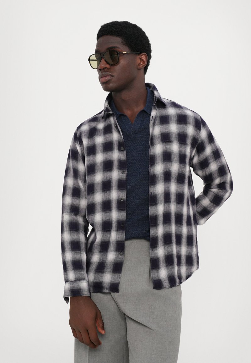 Button-up flanellen shirt in een marineblauw en wit geruit patroon, gecombineerd met een marineblauwe textuurgebreide shirt. Past goed bij lichtgrijze broeken.