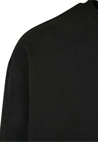 Felpa nera con scollatura a girocollo a coste, realizzata in tessuto testurizzato; presenta una vestibilità rilassata e cuciture lisce, evidenziando un design minimalista.