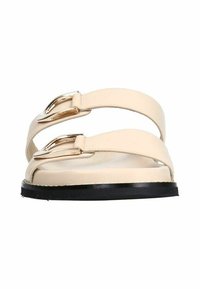 Des sandales en cuir beige présentent deux larges sangles avec des boucles dorées et une semelle en caoutchouc noire. Semelle plate pour un confort et une stabilité optimaux.